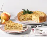 Un délicieux gâteau aux pommes, garni d'amandes effilées, est présenté avec une part déjà coupée. Des pommes fraîches sont disposées à côté.