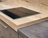 Eine moderne Küche mit einer Holzoptik-Arbeitsplatte und einem dunklen Stein-Arbeitsplatten-Material. Ein Kochfeld ist eingelassen.