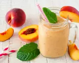 Erfrischender Pfirsich Smoothie im Glas, garniert mit Minze und Pfirsichspalten. Dazu frische Pfirsiche und Trinkhalme.
