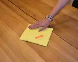 Hand wischt mit gelbem Tuch über Holzoberfläche, um den holztisch aufhellen.
