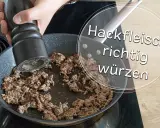 Hand würzt Hackfleisch in Pfanne. Die Frage "wieviel Salz auf ein Kilo Hackfleisch" wird hier visuell beantwortet: richtig würzen!