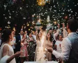 Eine ausgelassene Hochzeitsparty statt einer steifen Feier! Gäste werfen Schmetterlinge und zünden Wunderkerzen an, während das Brautpaar vor einem beleuchteten Kuchen steht.