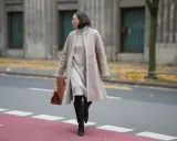 A woman demonstrates how to layer a dress for winter with a cozy turtleneck dress, a shearling coat, and stylish boots.