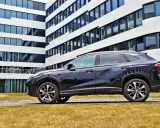 Czarny SUV MG HS, z nowoczesnym designem, zaparkowany przed biurowcem. Jego linia nadwozia sugeruje dynamiczne osiągi i niskie spalanie.