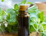 Brązowa buteleczka olejku z oregano, otoczona świeżymi gałązkami tej aromatycznej rośliny. Idealny do naturalnych zastosowań.