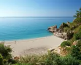 Playa de Burriana: Ein sonniger Strand mit türkisfarbenem Wasser, Felsen und üppiger Vegetation. Einige Menschen genießen die Ruhe.