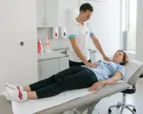 Fizjoterapeuta pomaga pacjentce w ćwiczeniach oddechowych, kładąc dłonie na jej klatce piersiowej i brzuchu.