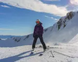 Narciarka w fioletowej kurtce i goglach stoi na ośnieżonym szczycie góry.