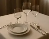 Un verre à eau, deux verres à vin vides, assiettes, couverts et une serviette sur une table dressée.
