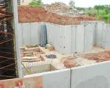Construcción de un muro de contención con paneles prefabricados de hormigón. Se observan tuberías y materiales de construcción en el sitio.