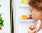 Kobieta zastanawia się nad wyborem zdrowych produktów do lodówki, jakby planowała dietę wojskową. Widać świeże warzywa i owoce.