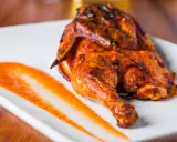 Un délicieux poulet portugais au four, la peau dorée et croustillante, servi avec une sauce épicée sur une assiette blanche.