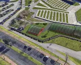 Vista aérea de un complejo deportivo con dos invernaderos verdes y una zona de aparcamiento. El **parque de las llamas** se extiende hasta la carretera.