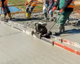 Budowlańcy używają wibrołaty do wyrównania świeżego betonu na budowie.