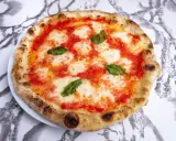 Pyszna pizza napoletana z pomidorami, mozzarellą i bazylią na białym talerzu, na tle marmurowego wzoru.