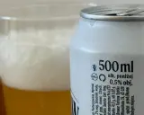 Piwo z puszki z etykietą "alk. poniżej 0,5% obj." obok szklanki z pianką. Sprawdzamy, ile promili ma to piwo.