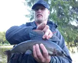 Man med keps och glasögon håller upp en fin fisk, fångad vid fiske i Sorsele.