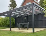 En mörk paviljong på en träaltan med bord och stolar. Perfekt för fika i trädgården.