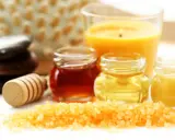 Ingredientes para un exfoliante corporal casero: sales, miel, aceites y una vela aromática.