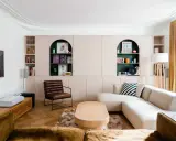 Un salon moderne avec un canapé beige, une chaise en cuir marron et des étagères murales roses. Quelle couleur pour une grande pièce à vivre ? Le vert émeraude des niches apporte une touche audacieuse.