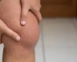 Dłoń uciska kolano, wskazując na ból z tyłu kolana.