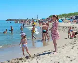 Słoneczne wczasy pod gruszą na plaży. Ludzie kąpią się w morzu i opalają na piasku. Dzieci bawią się w wodzie i budują zamki z piasku.