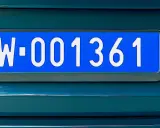Niebieskie tablice rejestracyjne z numerem W-001361 na ciemnozielonym samochodzie.