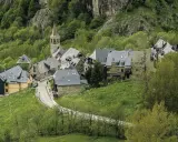 Pueblos del Valle de Arán, con casas de piedra y tejados grises, se asoman entre la vegetación verde y un camino serpenteante.