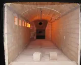 Wnętrze krematorium, gdzie czeka całun do kremacji. Pomieszczenie wyłożone cegłami, z łukowym sklepieniem i widocznym otworem pieca.