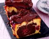 Zwei Stücke saftiger Marmorkuchen mit Kirschen und Schokoladenglasur auf einem dunklen Brett.