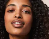 Ein Porträt einer Frau mit voluminösen, dunklen Locken, die die Curly Girl Methode perfektioniert. Ihre Haut strahlt, ihre Augen funkeln.