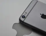 Srebrny iPhone leży na tle z wyciętym logo Apple, symbolizując spójność ekosystemu Apple.