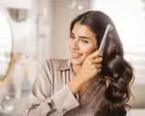 Donna sorridente si pettina i capelli scuri e ondulati, che appaiono lucidi come dal parrucchiere.