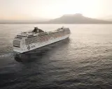Kryssningsfartyget MSC Poesia glider fram på havet i solnedgången, med en vulkan i bakgrunden.
