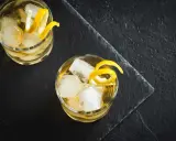 Zwei erfrischende Whiskey Cocktails mit Eis und Zitronenzesten auf dunklem Stein.