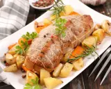 Rôti de veau savoureux, entouré de pommes de terre rôties, carottes et herbes aromatiques, prêt à être dégusté.