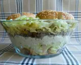 Warstwowa sałatka big mac w szklanej misie, z bułkami na wierzchu.