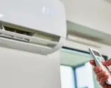 Mano con control remoto ajustando el aire acondicionado a 21 grados. ¿Es mejor apagar el aire acondicionado o dejarlo encendido?