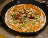 Ein authentisches Butter Chicken Rezept original in einer Gusseisenpfanne, garniert mit Koriander und gehackten Mandeln.