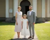 Elegancki strój rodziców na komunię dziecka: mama w jasnej sukience, tata w szarym garniturze, obok córka w bieli.