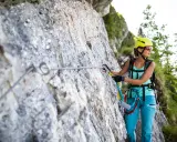 Kobieta w kasku i sprzęcie wspinaczkowym pokonuje via ferrata polska. Wspinaczka po skalnej ścianie z liną asekuracyjną.