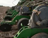 A row of green planters sits in a field, ready for planting. These machines are essential for farmers, contributing to the average hours on a tractor per year.