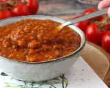 Une cuillère prélève une portion généreuse de sauce bolognaise maison, riche et savoureuse, dans un bol. Des tomates fraîches en arrière-plan.