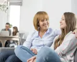 Madre e figlia sorridono, un momento di complicità che contrasta con il distacco emotivo dai figli in lontananza.