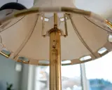 Detaljbild av en golvlampa i mässing från Ateljé Lyktan. Skärmen är av tyg med mässingsdetaljer.