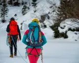 Dwóch alpinistów w zimowych strojach, z plecakami i sprzętem, przemierza ośnieżony teren. To inspiracja, co zabrać w góry zimą.