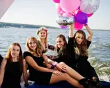 Uśmiechnięte kobiety na łodzi z balonami, celebrujące organizację wieczoru panieńskiego.