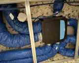 Système VMC installé dans un faux plafond. Les gaines bleues isolées sont connectées à une unité centrale noire. Un bon choix de VMC est essentiel pour la qualité de l'air intérieur.