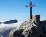 Krzyż na skalistym szczycie Gerlach. Widok na Tatry Wysokie ponad morzem chmur.