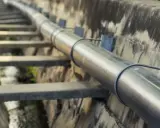 Długi, metalowy rurociąg biegnie wzdłuż betonowego koryta. To ważna kanalizacja tłoczna, transportująca płyny.